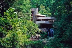 a house in the middle of some trees with a waterfall running between it's sides