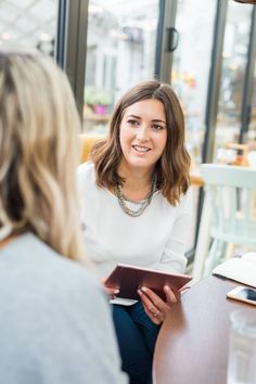 two women are sitting at a table and one is looking at the other woman's tablet