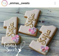 three decorated cookies with pink and gold frosting are on a wooden table next to each other