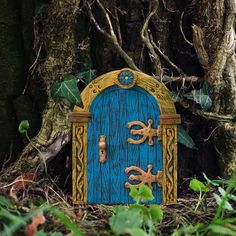 a small blue and yellow door in the grass next to a tree with leaves on it