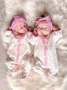 two baby babies laying on top of a white rug next to each other with pink bows