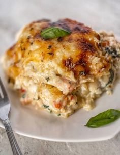 a white plate topped with lasagna covered in cheese and herbs next to a fork