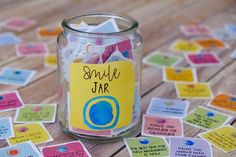 a jar filled with lots of stickers on top of a wooden table covered in notes