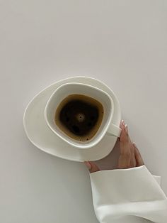 a person holding a coffee cup in their left hand on top of a saucer