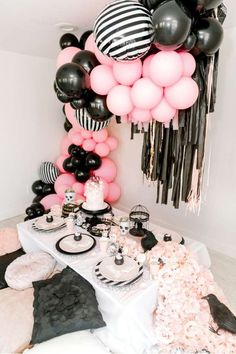 a table topped with black and white balloons next to a tall column of pink and black balloons