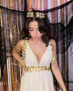 a woman in a white dress with gold jewelry on her head and hands behind her back