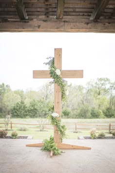 a wooden cross with flowers and greenery on it in the middle of an open area