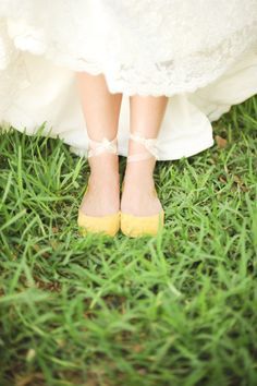 the bride's yellow shoes are tied to her wedding dress and she is standing in the grass