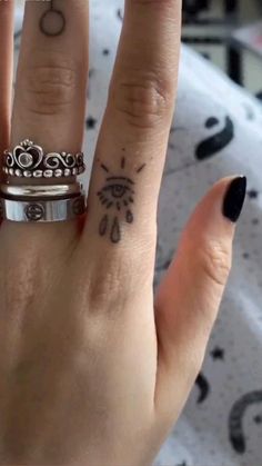 a woman's hand with two rings on it and a tattoo design on the middle finger