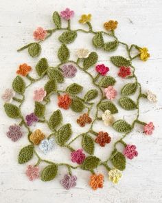 crocheted leaves and flowers arranged on a white surface with small holes in the middle