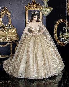 a woman in a gold gown and tiara standing next to a chair with a chandelier