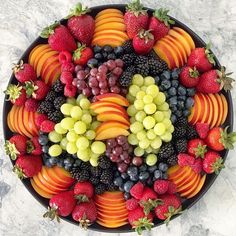 a platter filled with assorted fruit on top of a marble countertop next to sliced strawberries, grapes, and peaches