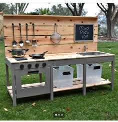 an outdoor kitchen with pots and pans on the stove top, outside in grass