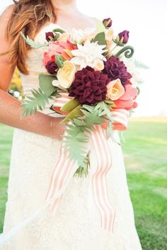 a woman holding a bouquet of flowers in her hand and wearing a white dress with red stripes