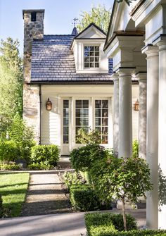 a white house with columns and windows on the front porch is surrounded by greenery