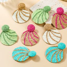 four handmade earrings with different colors and designs on top of a beige table next to a white plate