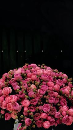 a vase filled with pink flowers on top of a white table next to a black wall