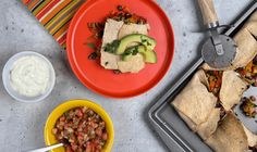 two plates with food on them next to some bowls and utensils, one has an avocado