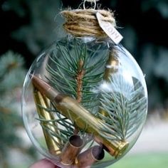 a hand holding a glass ornament with a pine branch and cinnamon stick in it