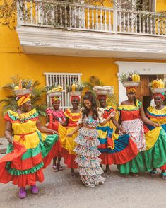 a group of women in colorful dresses standing next to each other near a yellow building