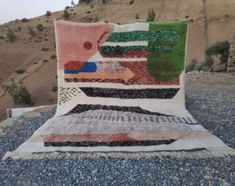 a patchwork quilt sitting on top of a pile of gravel next to a hill