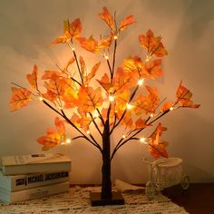 a lighted tree is sitting on a table next to some books and a lamp that looks like leaves