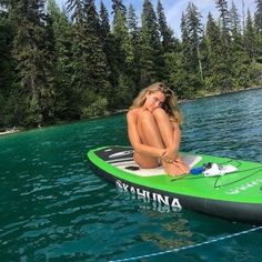 a woman sitting on top of a surfboard in the water next to some trees