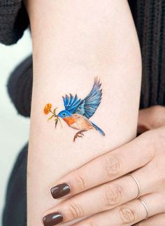 a woman's arm with a small blue bird tattoo on the left side of her arm