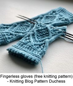 two knitted gloves sitting next to each other with knitting needles in front of them