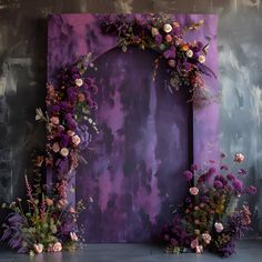 a purple backdrop with flowers and greenery on the floor next to an empty frame