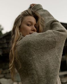 a woman with long hair is holding her arms behind her head and looking off to the side