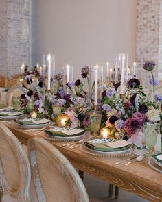 the table is set with candles, plates and vases filled with purple flowers on them