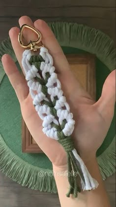 a hand holding a keychain that is made out of white and green yarn