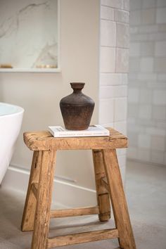 a vase sitting on top of a wooden stool next to a bath tub