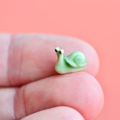 a tiny green snail sitting on top of a persons finger in front of a pink background