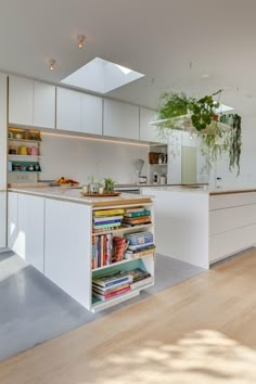 a kitchen with white cabinets and an island in the middle is filled with books as well as plants