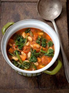 a white bowl filled with vegetable soup on top of a wooden table next to a spoon