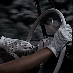 a man driving a car with his hand on the steering wheel while wearing white gloves