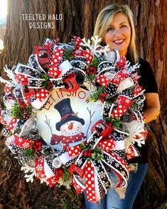 a woman standing in front of a tree holding a wreath with snowman on it