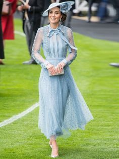 a woman in a blue dress and hat walks on the grass with other people behind her