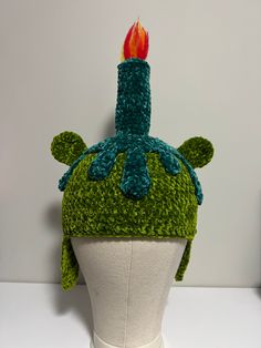 a green knitted hat with a lit candle on it's head, sitting on top of a white mannequin