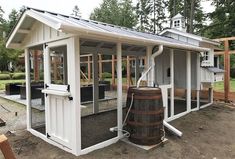 a small white building with a large barrel in front of it and some trees behind it