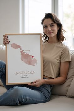 a woman sitting on a couch holding up a framed poster with the state of maine