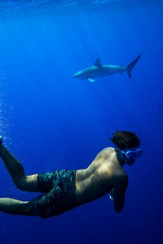 a man swimming in the ocean with a shark behind him