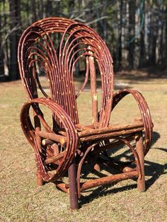 a wooden chair made out of sticks and wickers on the grass in front of some trees