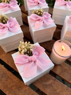 several small boxes with pink bows are sitting on a table next to a candle