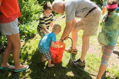 a group of people standing around a little boy in a red bucket with water on it