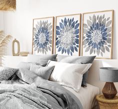 two blue and white flower paintings on the wall above a neatly made bed with pillows