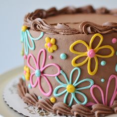 a chocolate cake decorated with colorful flowers and icing on a white doily plate