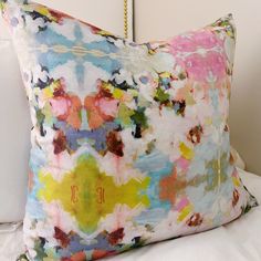 a colorful pillow sitting on top of a bed next to a white headboard and pillows